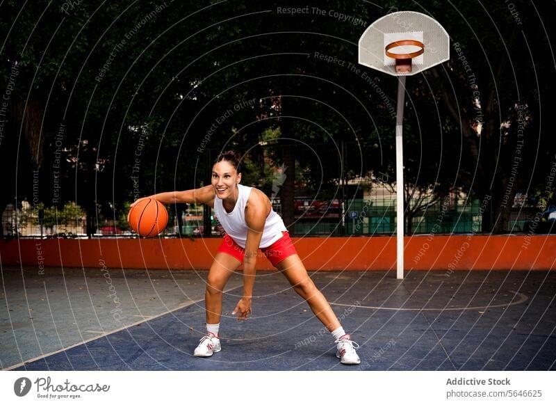 Full body of sporty happy young female in activewear looking away while playing basketball on court during sunny summer day Sportswoman Basketball Play Court