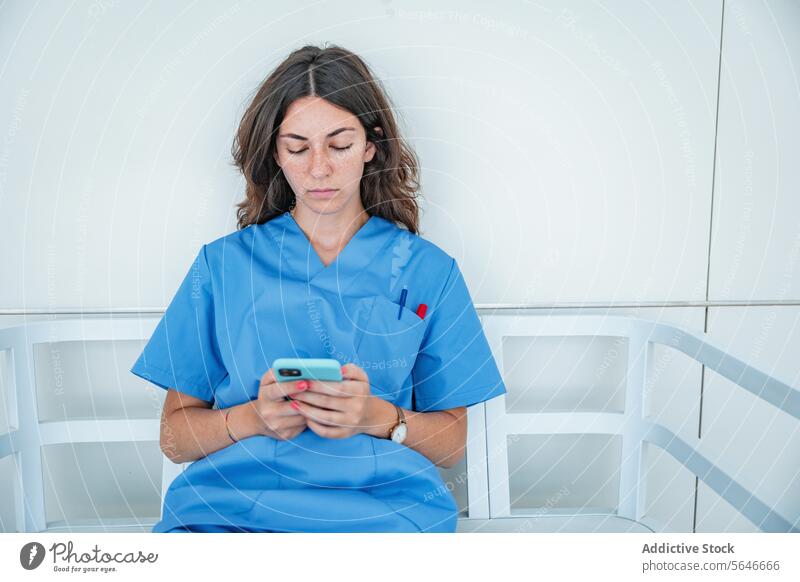 Young female nurse browsing smartphone while sitting on bench woman hospital using uniform medicine relax gadget device mobile medical connection cellphone