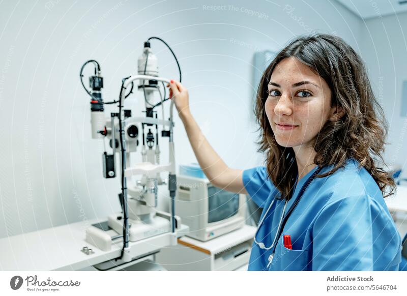 Happy young woman doctor standing near slit lamp biomicroscope in hospital smile happy uniform stethoscope illuminate pen female professional specialist work