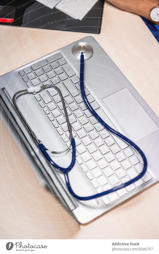 Unrecognizable doctor with stethoscope on laptop sitting at table in light person work document professional illuminate clinic medical device gadget job