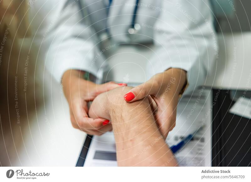 Unrecognizable woman doctor examining anonymous patient hand at consultation table stethoscope clinic check up pulse hospital female nail polish pen clipboard