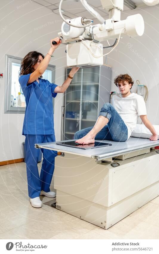 Young female technician adjusts X Ray machine for scanning patient sitting on bed in clinic woman nurse x ray hospital diagnosis health care medicine