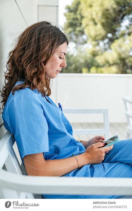 Young female nurse browsing smartphone while sitting on bench woman hospital using uniform medicine relax gadget device mobile medical connection cellphone