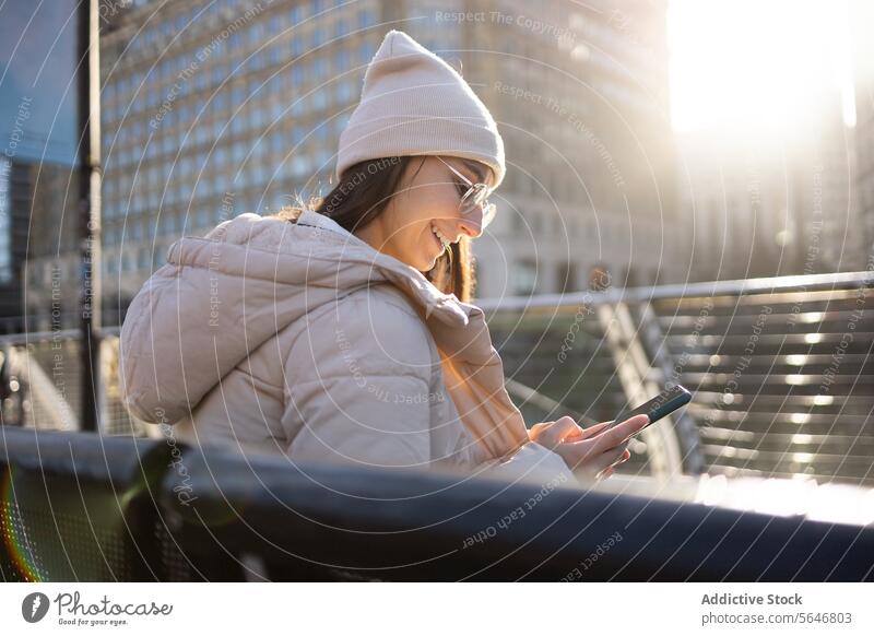 Happy woman in warm clothes using mobile phone in city tourist smartphone smile browsing happy trip vacation female young hat cheerful building travel gadget