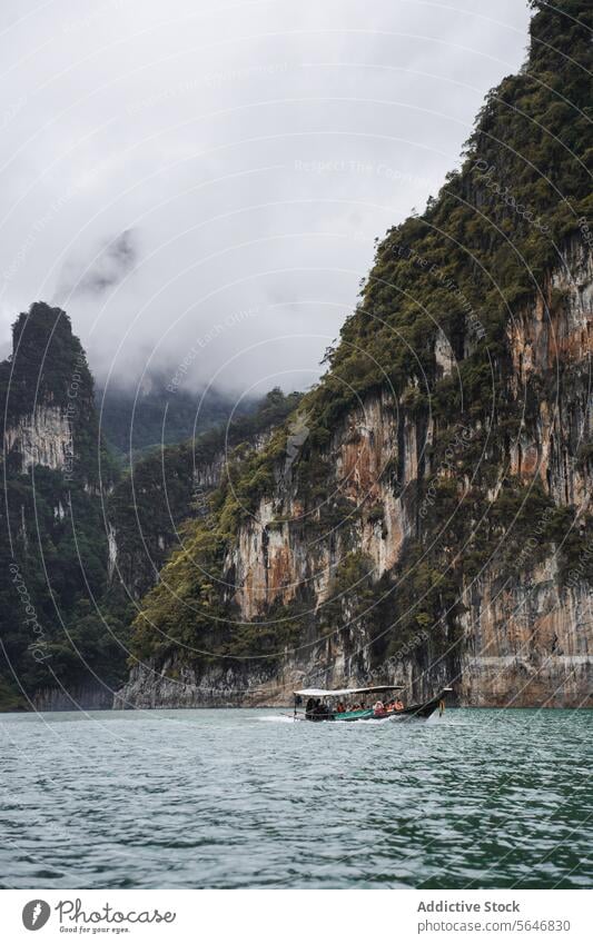 Boat floating on rippling lake near high mountains in Thailand boat people tourist travel rocky nature cloud greenery cheow lan lake thailand asia scenic cliff