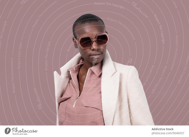 Thoughtful young bold African American female model in trendy outfit and sunglasses looking away on pink background Woman Trendy Style Outfit Sunglasses Model