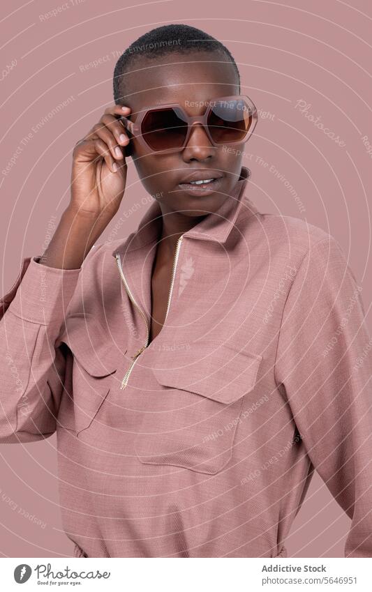 Young bold African American female model in stylish pink clothes and sunglasses standing looking away against pink background Woman Style Trendy Outfit Pink