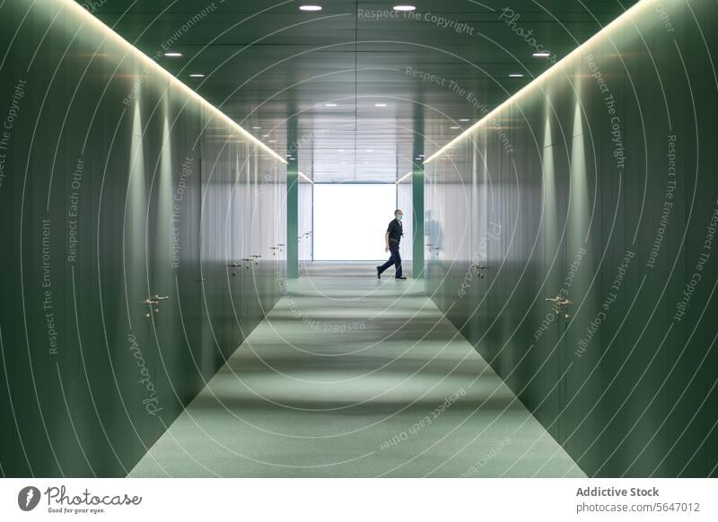 Side view of anonymous Man walking in illuminated passage with green walls in modern hospital Hospital Passage Ceiling Light Interior Green Modern Medical Clean