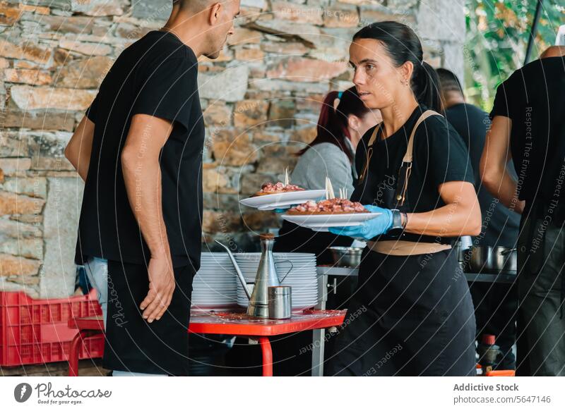 Waitress in blue gloves carrying plates with cooked octopus serving Galician food festival fresh server bustling atmosphere traditional dishes kitchen table