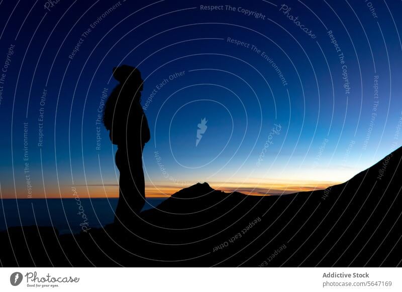 Silhouette of unrecognizable traveler admiring orange sunset on highland person cliff silhouette mountain admire blue sky nature trip journey sundown stand