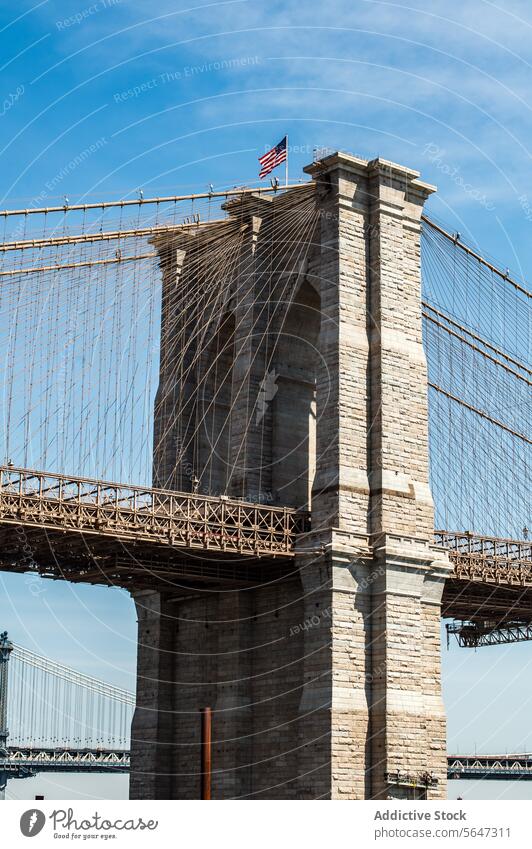 Brooklyn Bridge tower with waving American flag against blue sky. brooklyn bridge american architecture iconic landmark new york cables stone clear historical