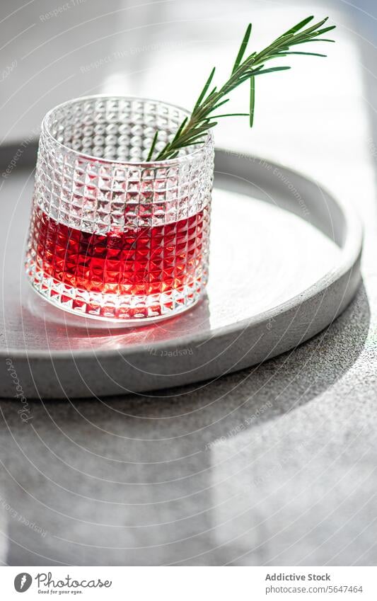Elegant cocktail with cherry and apple juice mixed with vodka garnished with a fresh rosemary sprig presented on a circular tray alcohol drink herb presentation