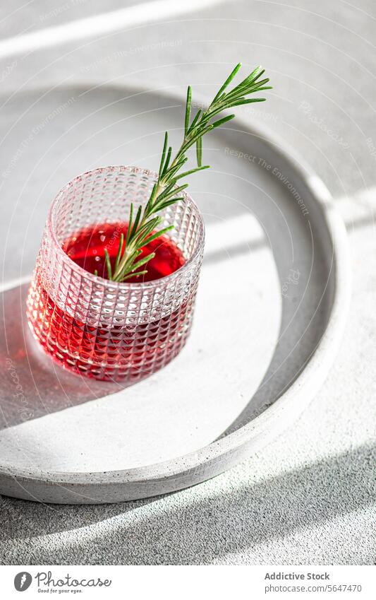 Top view of elegant cocktail with cherry and apple juice mixed with vodka garnished with a fresh rosemary sprig presented on a circular tray alcohol drink herb