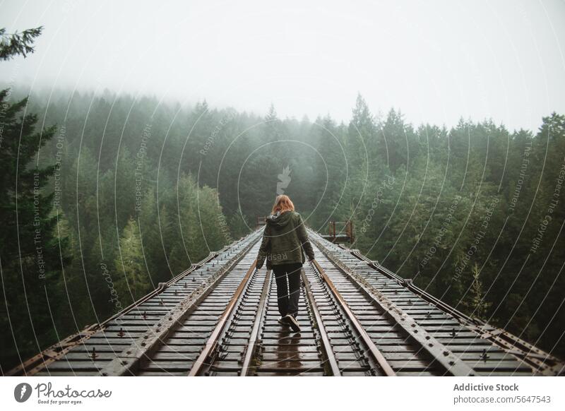 Woman walking in misty forest railroad on Vancouver Island woman person fog adventure mystery back view vancouver island british columbia canada greenery nature