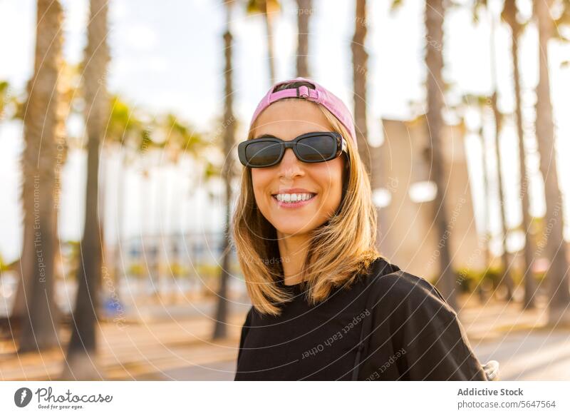 Happy beautiful female with blond hair woman sunglasses cap portrait smiling tshirt attractive black pink park happy blur enjoy headshot looking at camera