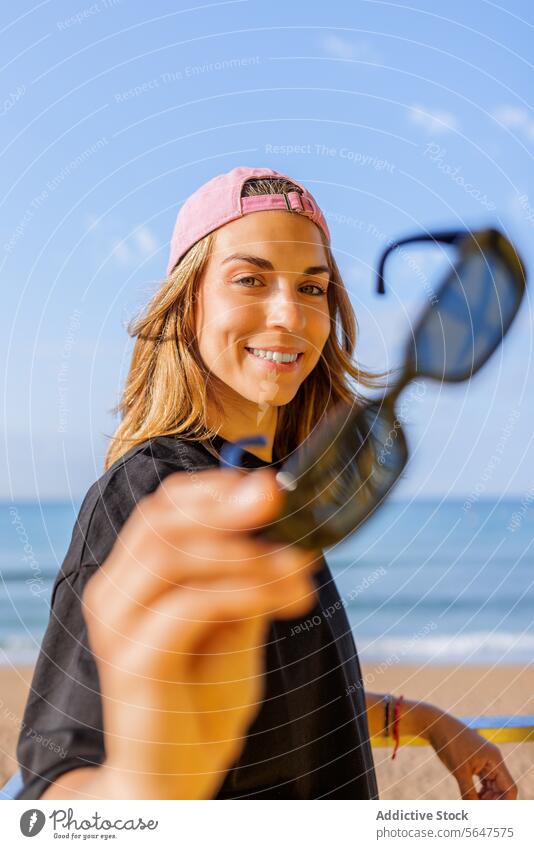 Smiling female at seaside during summer woman happy sunglasses cap showing portrait beach sky sunny lifestyle looking at camera stylish blond hair beautiful