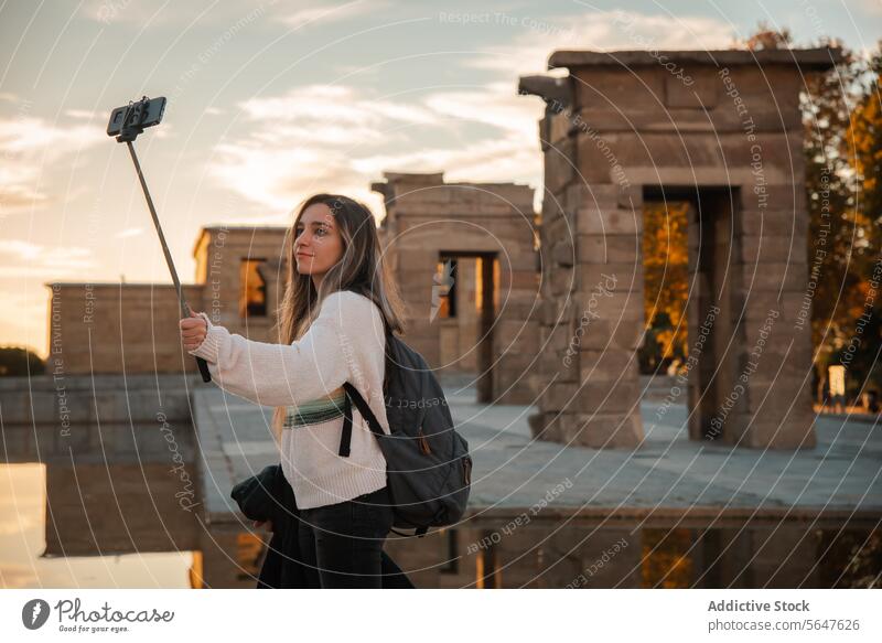 Young traveler taking a selfie at historical Debod Temple in Madrid woman historical site temple sunset phone selfie stick backpack tourism ancient architecture