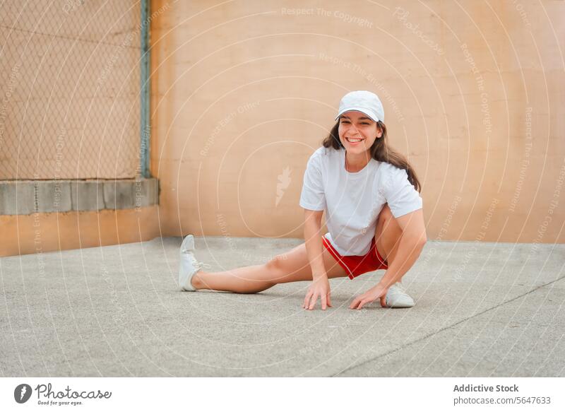 Active woman stretching outdoors in sporty attire active exercise fitness healthy lifestyle cheerful young athletic cap sports looking at camera clothing