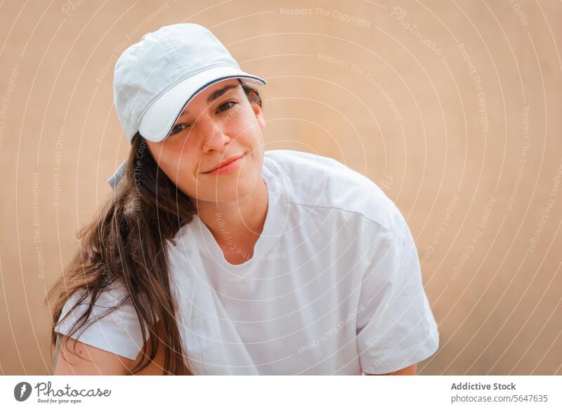 Casual woman smiling with white cap and shirt smile casual young relaxed beige looking at camera background lifestyle portrait fashion happy gentle simple