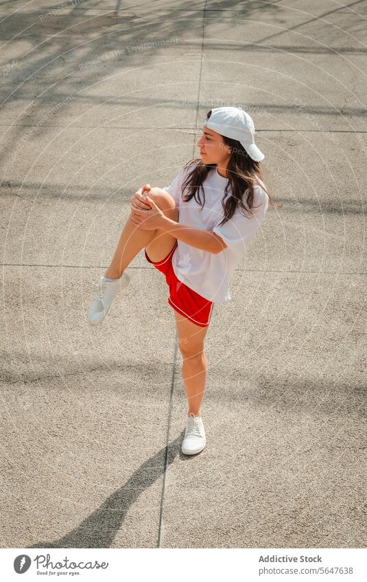 Active woman stretching outdoors on a sunny day sportswear cap red shorts workout fitness leg street daytime active health exercise young adult white shirt
