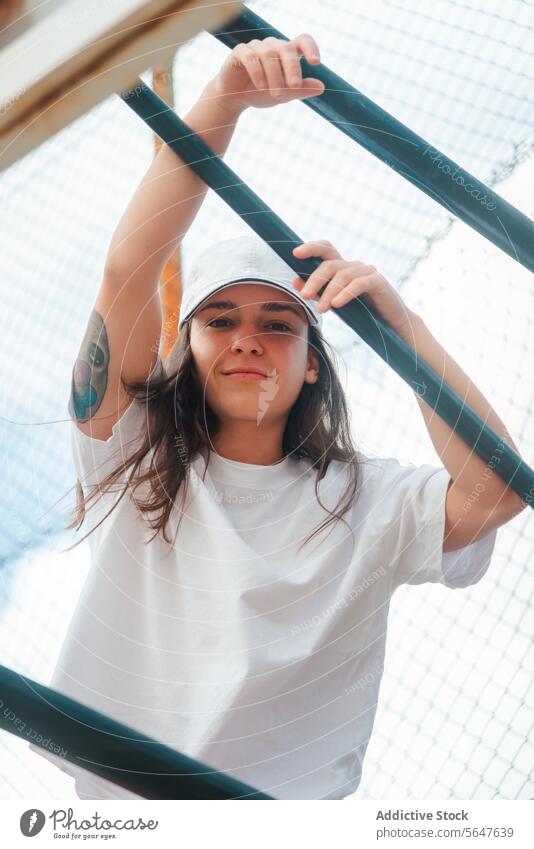 Casual Urban Style Young Woman by Metal Fence woman young tattoo casual style urban pose fence metal looking at camera green relaxed confident white tee