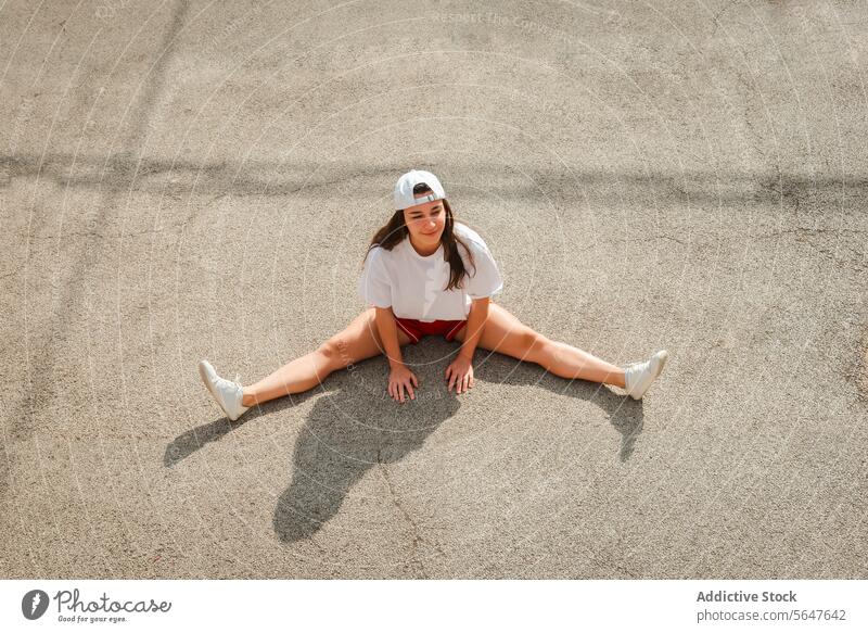 Young woman resting after workout on concrete ground young athletic outdoor cap sportswear sitting leisure active fitness exercise relax casual streetwear urban