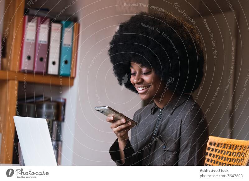 Cheerful black woman browsing smartphone online internet modern social media chat connection laptop surfing home female african american positive trendy gadget