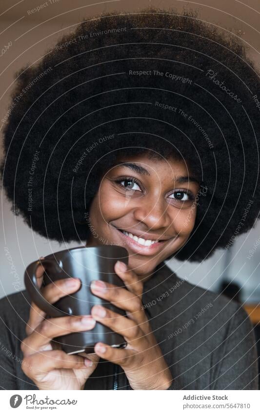 Positive black woman with hot beverage cup hot drink coffee afro feminine hairstyle dreamy smile appearance happy charming brunette attractive female cheerful