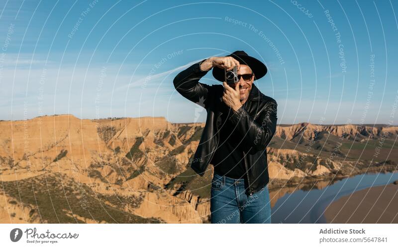 Photographer in leather jacket framing view with retro camera man happy photographer hat frame hands smiling scenic analog canyon blue sky stylish outdoor