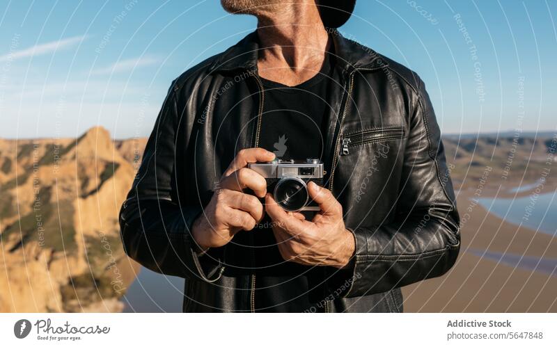 Stylish anonymous man exploring nature with a vintage camera photographer desert explorer cropped adventurer landscape stylish unrecognizable leather jacket