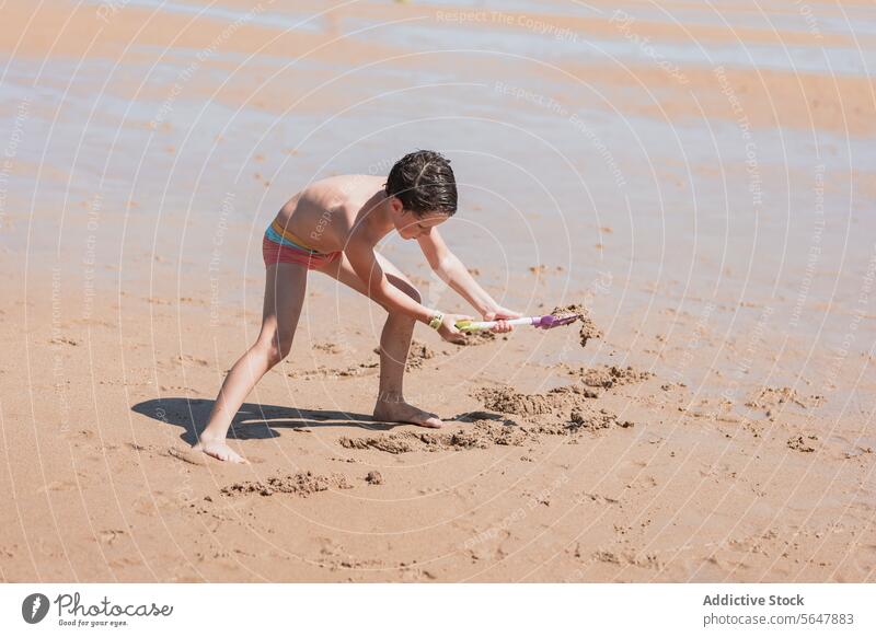 Young boy playing with a toy shovel on sandy beach ocean child digging seaside coast summer outdoor activity sunny seashore playful nature waterfront toddler