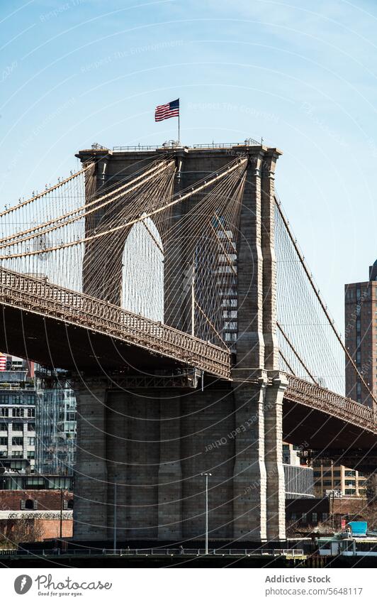 Brooklyn Bridge tower with waving American flag against blue sky. brooklyn bridge american architecture iconic landmark new york cables stone clear historical