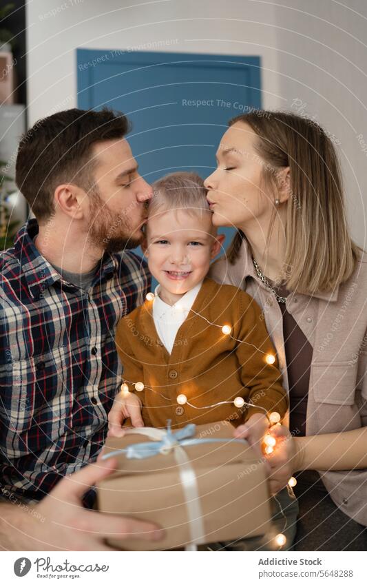 Parents giving their little boy a kiss against Christmas tree at home family child festive holiday season warmth couple love affection celebration cozy decor