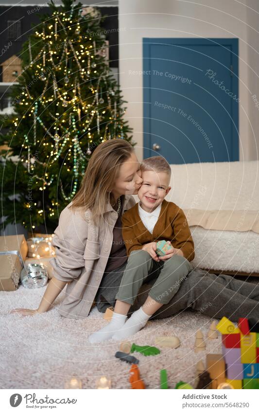 Mother kissing her son and playing together with wooden toys in living room against Christmas tree mother child joy laughter festive season family holiday