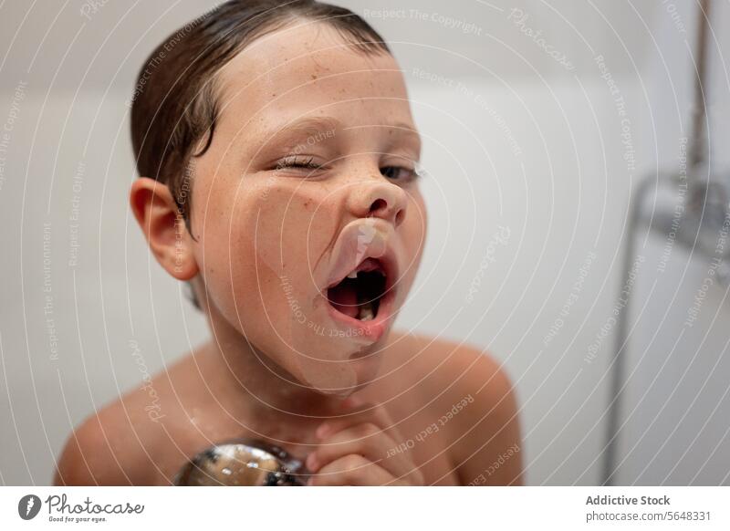 Little boy with wet hair making faces at glass wall in bathroom child shower playful hygiene kid funny little cute adorable having fun childhood grimace toddler