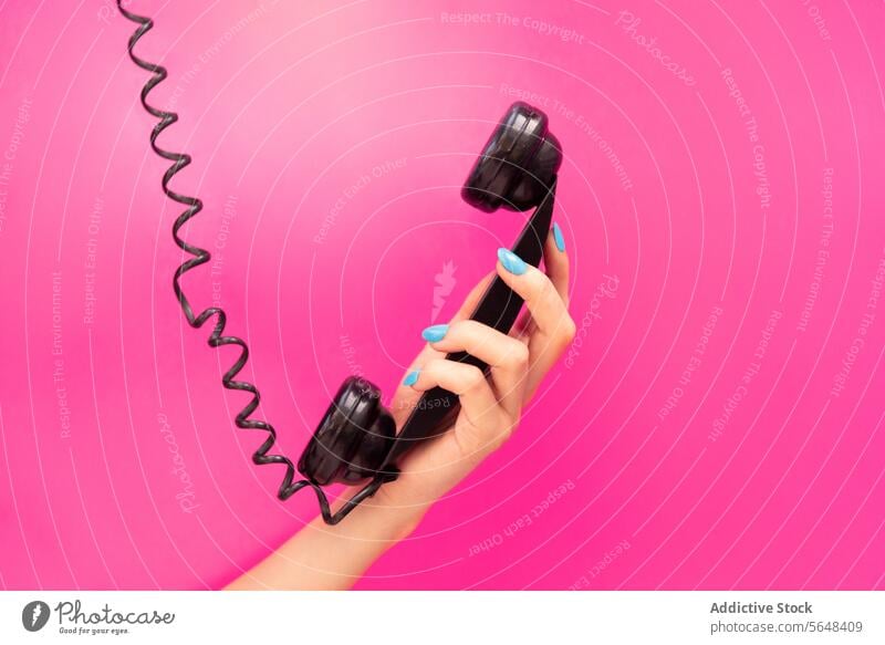 Hand of anonymous woman Holding Telephone Receiver hand holding telephone receiver black blue nail polish pink background vibrant communication call retro
