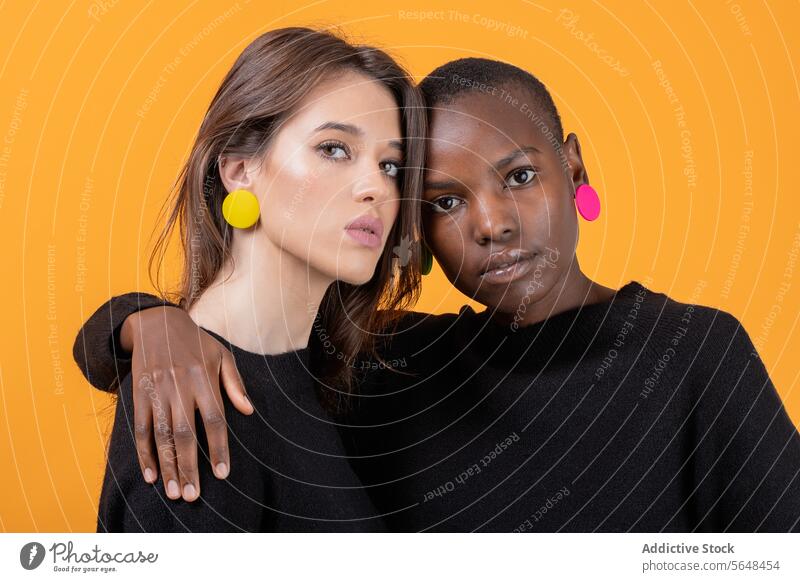 Diverse young female friends wearing colorful earrings embracing each other against yellow background women diverse confident portrait trendy tshirt together