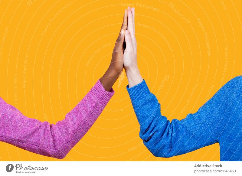 Anonymous multiracial women touching hands over yellow background diverse unity sweater together friend pink blue support crop collaborate community clasp