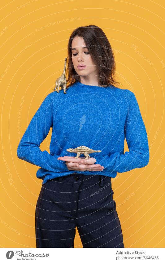 Woman with toy animals isolated over yellow background woman playful balance hand head portrait sweater blue childhood playing dinosaur representation leisure