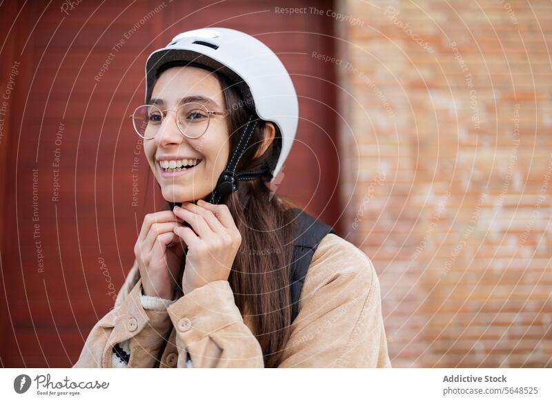 Smiling woman fastening bicycle helmet outdoors safety smile preparation strap securing brick wall ride cheerful young cyclist biking gear protective