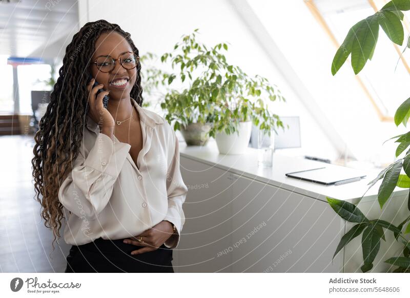 Thoughtful black businesswoman using smartphone in office Businesswoman Smartphone Using Office Smile Happy Hand On Stomach Afro Young Workplace Manager Plant