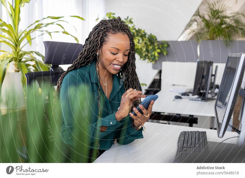 Happy black businesswoman using smartphone at desk in office Businesswoman Smartphone Using Desk Office Work Busy Touching Occupation Desktop PC Device Smile