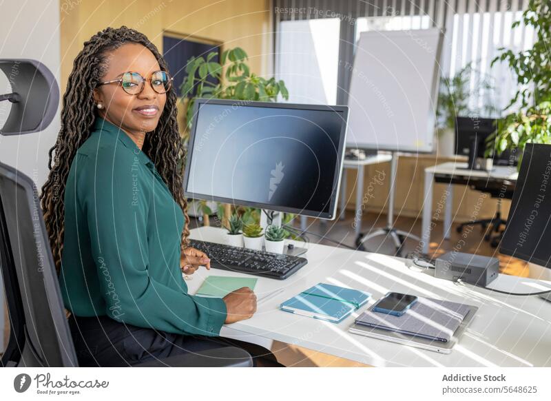 Happy businesswoman sitting at computer desk in office Businesswoman Portrait Computer Desk Office Confident Smile Monitor Eyeglasses Workplace Afro Copy Space