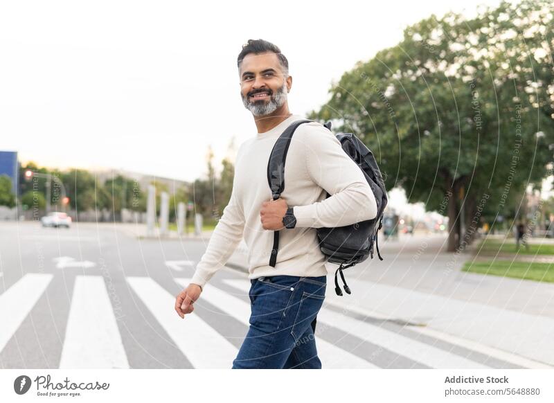 Happy Indian man in casual clothing with backpack looking away while crossing the street businessman beard city sweater walk smart adult urban entrepreneur