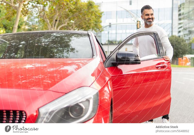 Glad ethnic driver getting in red automobile on street businessman car road trip ride entrepreneur commute transport vehicle male seat journey lifestyle beard