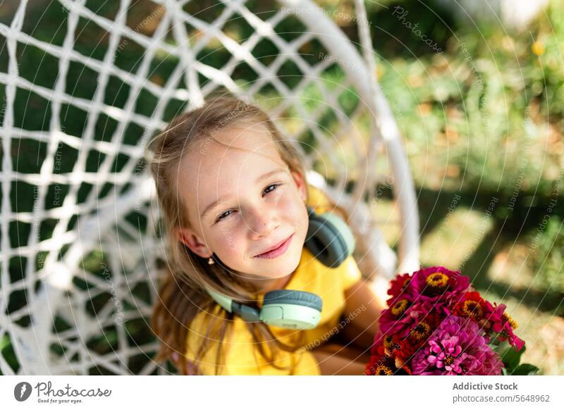 Young girl smiling with flowers in a hanging chair child smile happy bouquet headphones leisure outdoor garden relaxation joyful youth nature bright sunny day