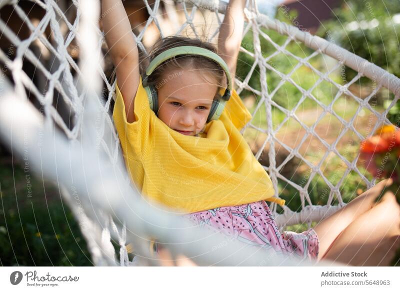 Young girl enjoying music in a backyard hammock child young relaxing headphones leisure outdoor sweater yellow comfort cozy enjoyment serene peaceful rest