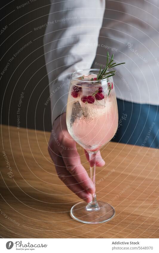 Rosemary winter cocktail garnished with cranberries rosemary cranberry drink glass stemware hand presentation cold refreshment sprig alcohol mixology bar
