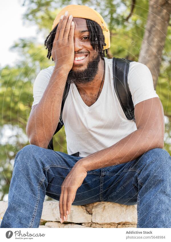 Cheerful black man covering eye in park hipster cover eye cover face half listen music headphones summer smile happy cool cheerful male young ethnic