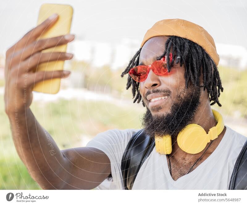 Cheerful male hipster taking selfie in park man using smartphone social media summer memory moment smile cool cheerful headphones young black ethnic